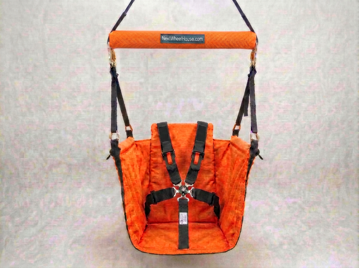 An orange swing seat with seatbelt, black harness straps and a padded top handle, shown against a light textured background. A brand label on the handle reads 'NewWheelhouse.